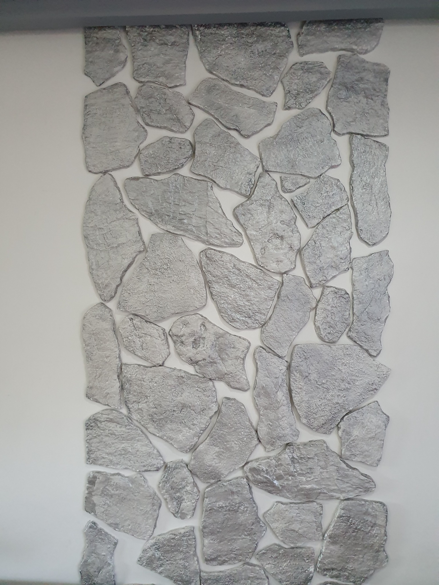 Dekoracyjna ściana we Wrocławiu z elementami imitującymi kamień w odcieniach szarości i srebra, ułożonymi na białym tle.