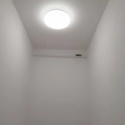 Wnętrze małego, pomalowanego na biało pomieszczenia z okrągłą lampą sufitową i rurą z zaworem przy suficie.