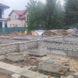RASBUD SPÓŁKA Z OGRANICZONĄ ODPOWIEDZIALNOŚCIĄ - Fundamenty z bloczków betonowych dla bliźniaka w Mirkowie, widoczne zbrojenia i palety z bloczkami. Na drugim planie budynki mieszkalne.