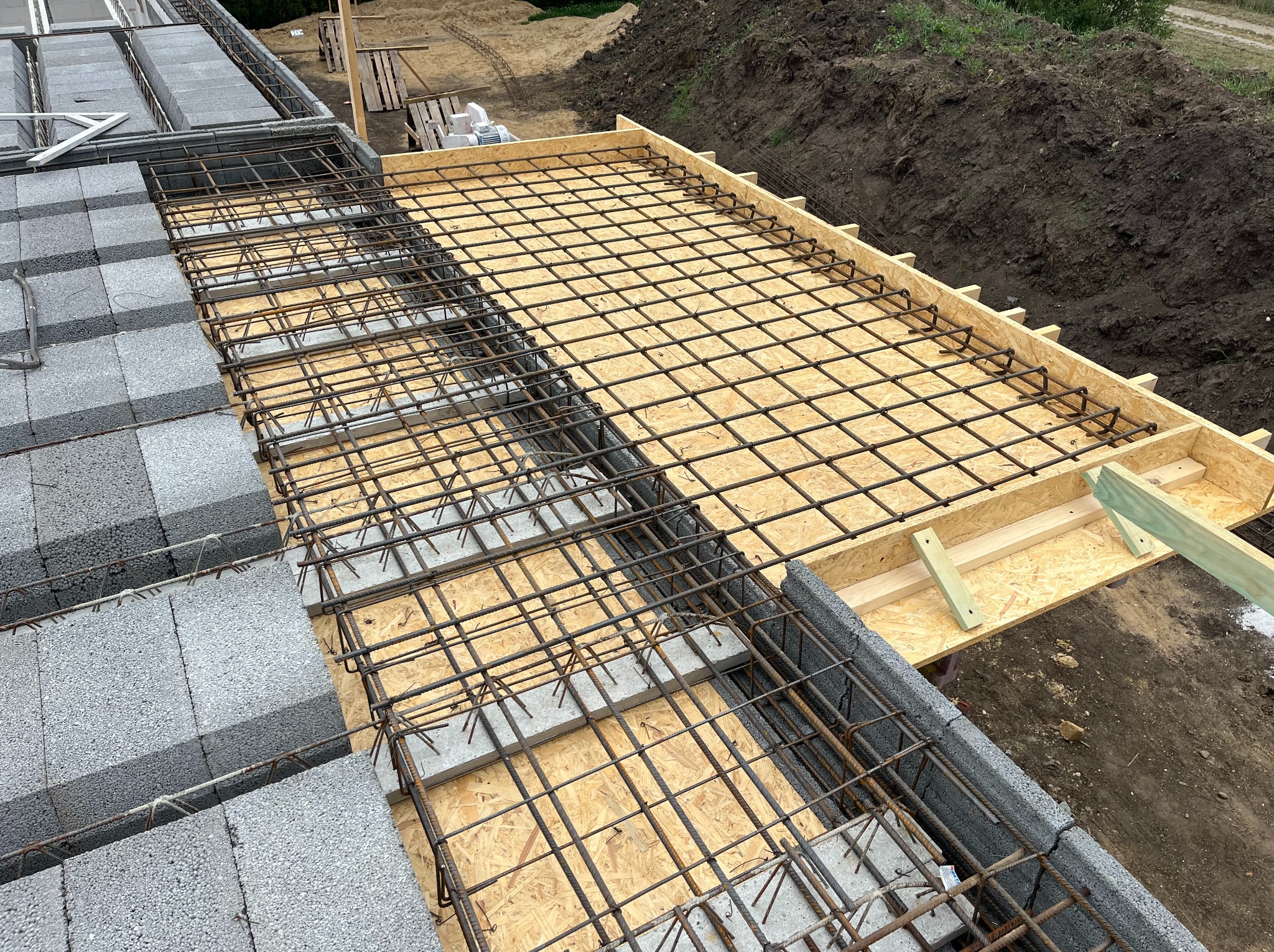 Zbrojenie stropu nad murowanymi ścianami z bloczków betonowych. Widoczna płyta OSB i drewniany szalunek. Budowa w stanie deweloperskim.