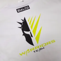 Biała koszulka z nadrukowanym czarno-żółtym logo przedstawiającym hełm wojownika i napis 'WARRIORS TEAM' oraz nazwą firmy 'BIALCO'.