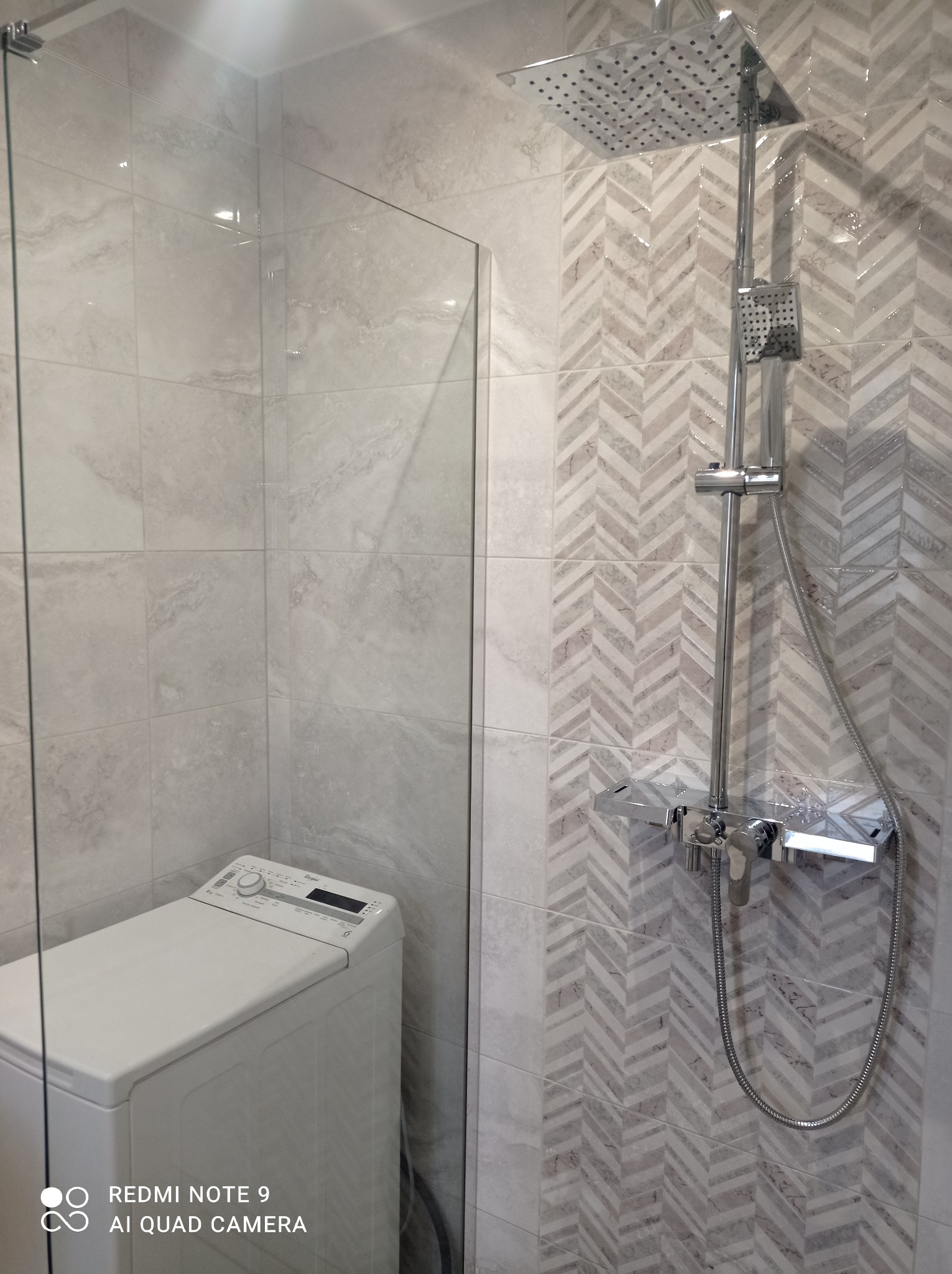 Wykończona łazienka w Grabowcu: kabina prysznicowa ze szklaną ścianką i deszczownicą na tle ściany z płytek w jodełkę. Pralka widoczna w rogu.