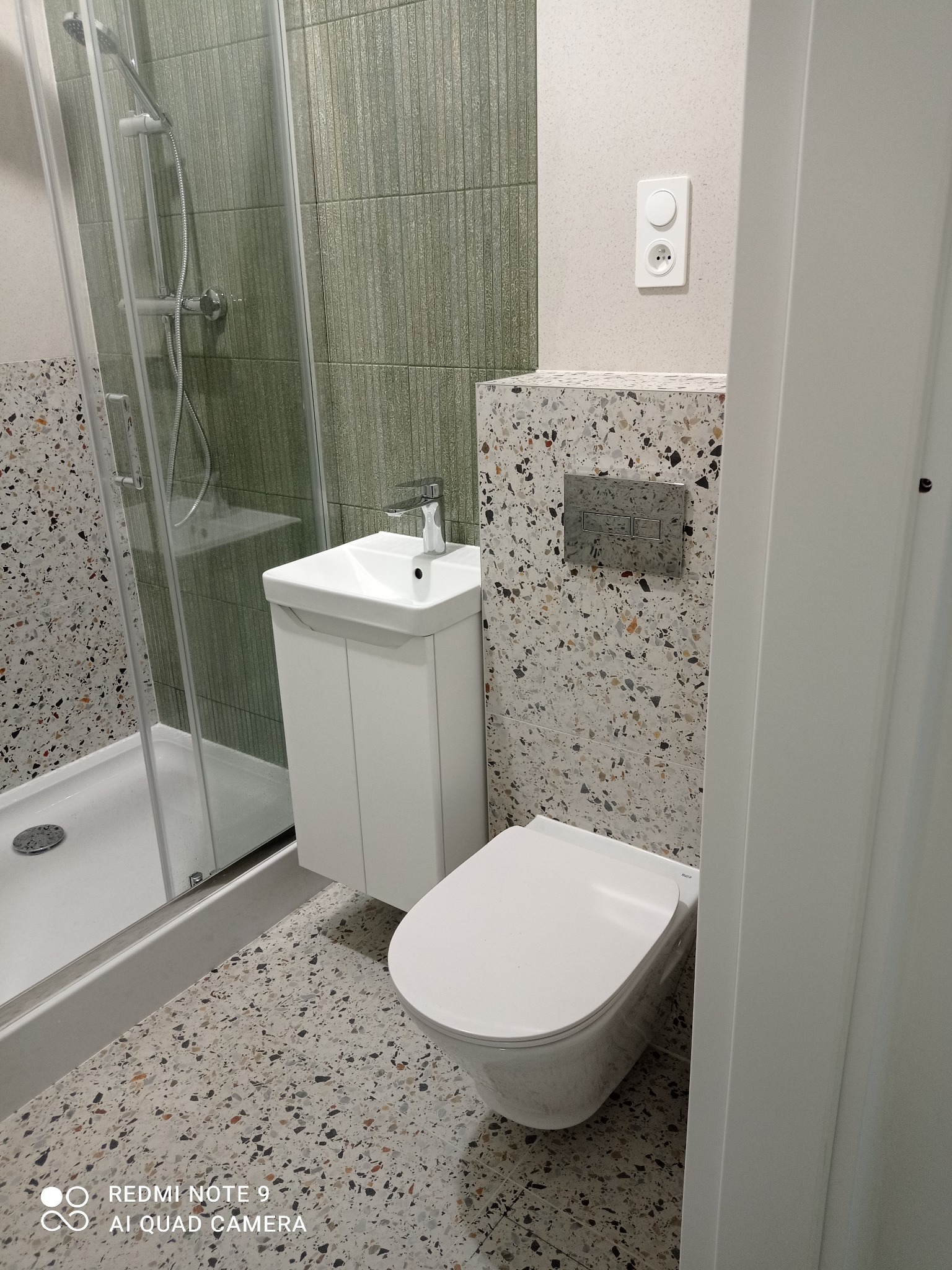 Nowoczesna łazienka z kabiną prysznicową, umywalką na szafce i podwieszaną toaletą. Płytki w stylu lastryko na podłodze i ścianie. Minimalistyczny design.