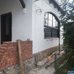 Prace przygotowawcze przed ociepleniem elewacji budynku w Słupsku, widoczny fragment ściany z cegły i kamienia, rusztowanie oraz nieporządek na posesji.