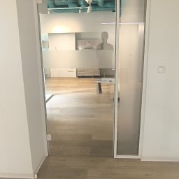 Dekor Mat Anna Parol - Szklane drzwi z matową folią w nowoczesnym biurze, widoczne rury pod sufitem i sylwetka osoby w tle.