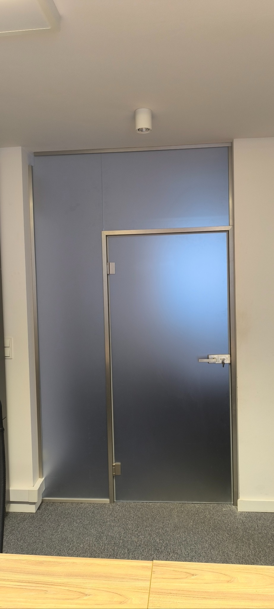 Szklane drzwi z matową powierzchnią i metalową ramą, zamontowane w biurze, widoczny zamek z kluczem.