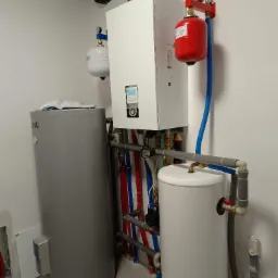 Instalacja kotła grzewczego z zbiornikami buforowymi i rurami w kolorach czerwonym i niebieskim, widoczne elementy zabezpieczone izolacją termiczną.