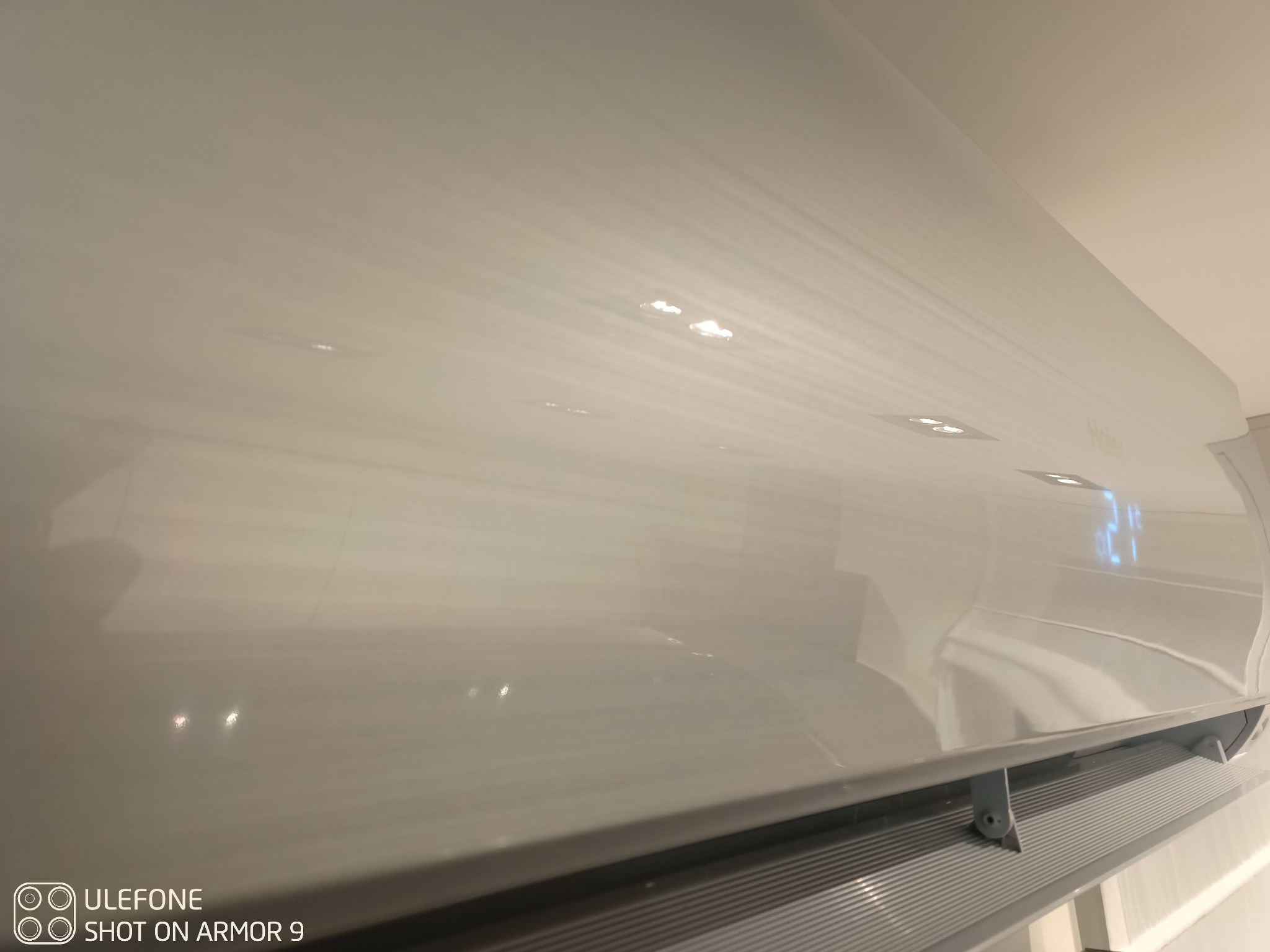 Biały klimatyzator marki Haier zamontowany na ścianie, widoczny wyświetlacz wskazujący temperaturę 21 stopni, dolna kratka wentylacyjna pod kątem.