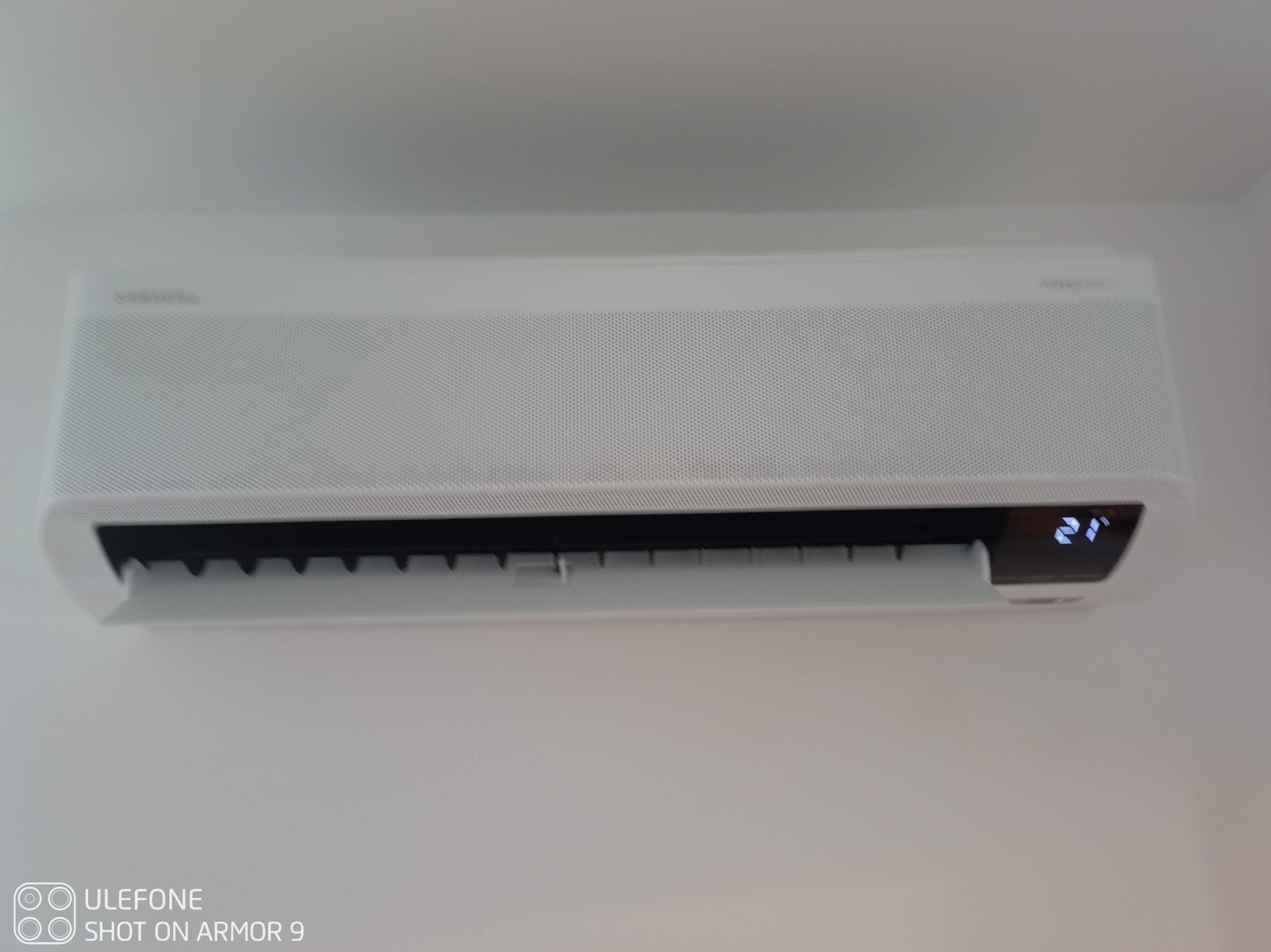 Biała jednostka klimatyzacji Samsung WindFree zamontowana na ścianie, wyświetlająca temperaturę 21 stopni Celsjusza.