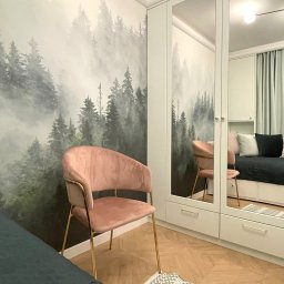 Pracownia Projektowa UNIQUE Anna Klimczewska-Waszczyk - Pokój z fototapetą leśną, różowym krzesłem na złotych nogach i szafą z lustrami. Widoczny fragment łóżka i dywanik. Jasne, naturalne światło.