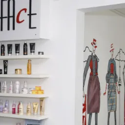 Wnętrze salonu fryzjerskiego: białe ściany, półki z kosmetykami do włosów marki L'Oreal, grafika przedstawiająca modelki w kapeluszach i sukienkach.