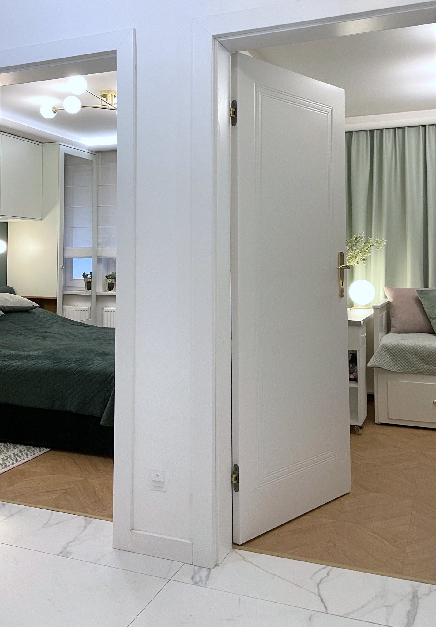 Otwarta biała, klasyczna  drzwi wewnętrzne, widok na sypialnię z zielonymi akcentami i parkietem. Białe płytki podłogowe w przedpokoju.