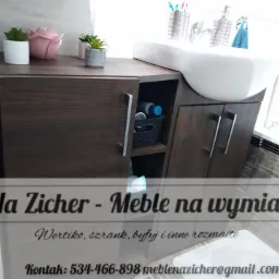 Szafka łazienkowa z ciemnego drewna pod umywalkę nablatową, z dekoracjami w postaci roślin w doniczkach i różowej figurki, widoczne akcesoria łazienkowe i ręcznik.