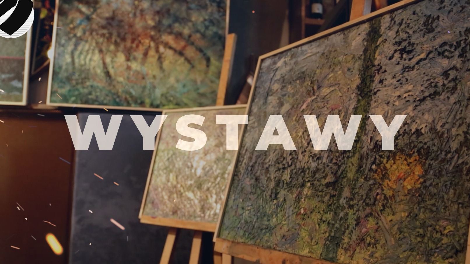 Ujęcie z pokazu malarstwa: rama obrazu na sztaludze z abstrakcyjnym malunkiem w odcieniach brązu i zieleni, z efektem iskier i napisem WYSTAWY.