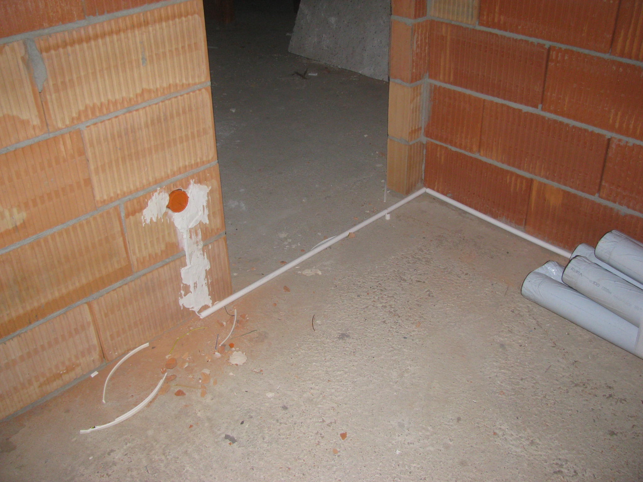 Surowy stan: ściany z pustaków, betonowa podłoga z rurami instalacyjnymi przy ścianie i wystającymi kablami z otworu w ścianie, przygotowanie do rozprowadzenia instalacji.