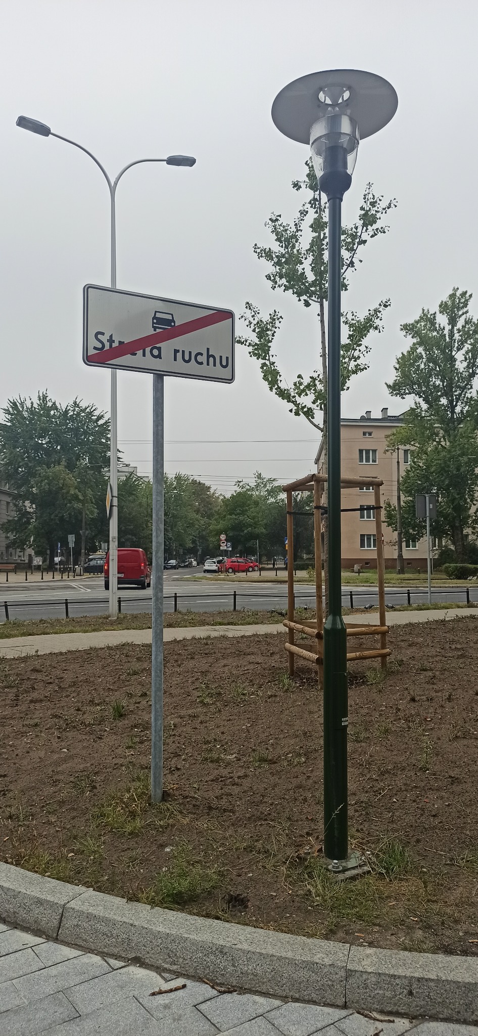 Miejska lampa uliczna z okrągłym kloszem i znakiem drogowym strefa ruchu, widok z poziomu gruntu.