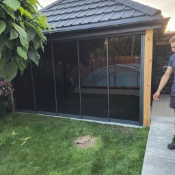 WFmontaż - Zadaszony taras z przesuwnymi szklanymi panelami w ogrodzie, widoczny fragment basenu i osoba w tle.