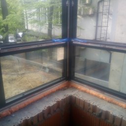 WFmontaż - Narożne okno z czarną ramą, uszczelnione pianką montażową, widok z zewnątrz na budynek i zieleń.