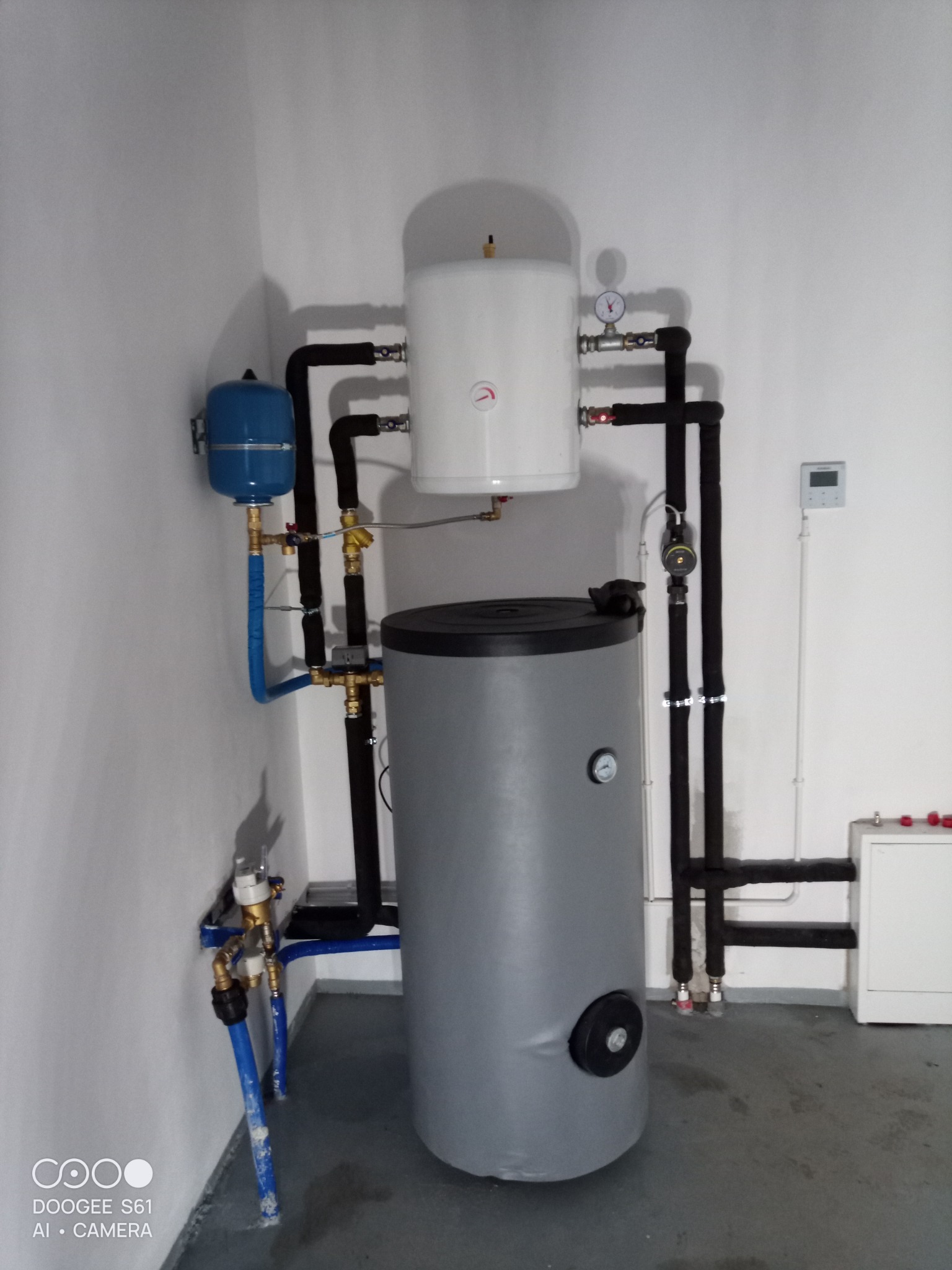 Szary zbiornik akumulacyjny ciepła z białym zasobnikiem i niebieskim naczyniem przeponowym, połączone rurami w kotłowni.