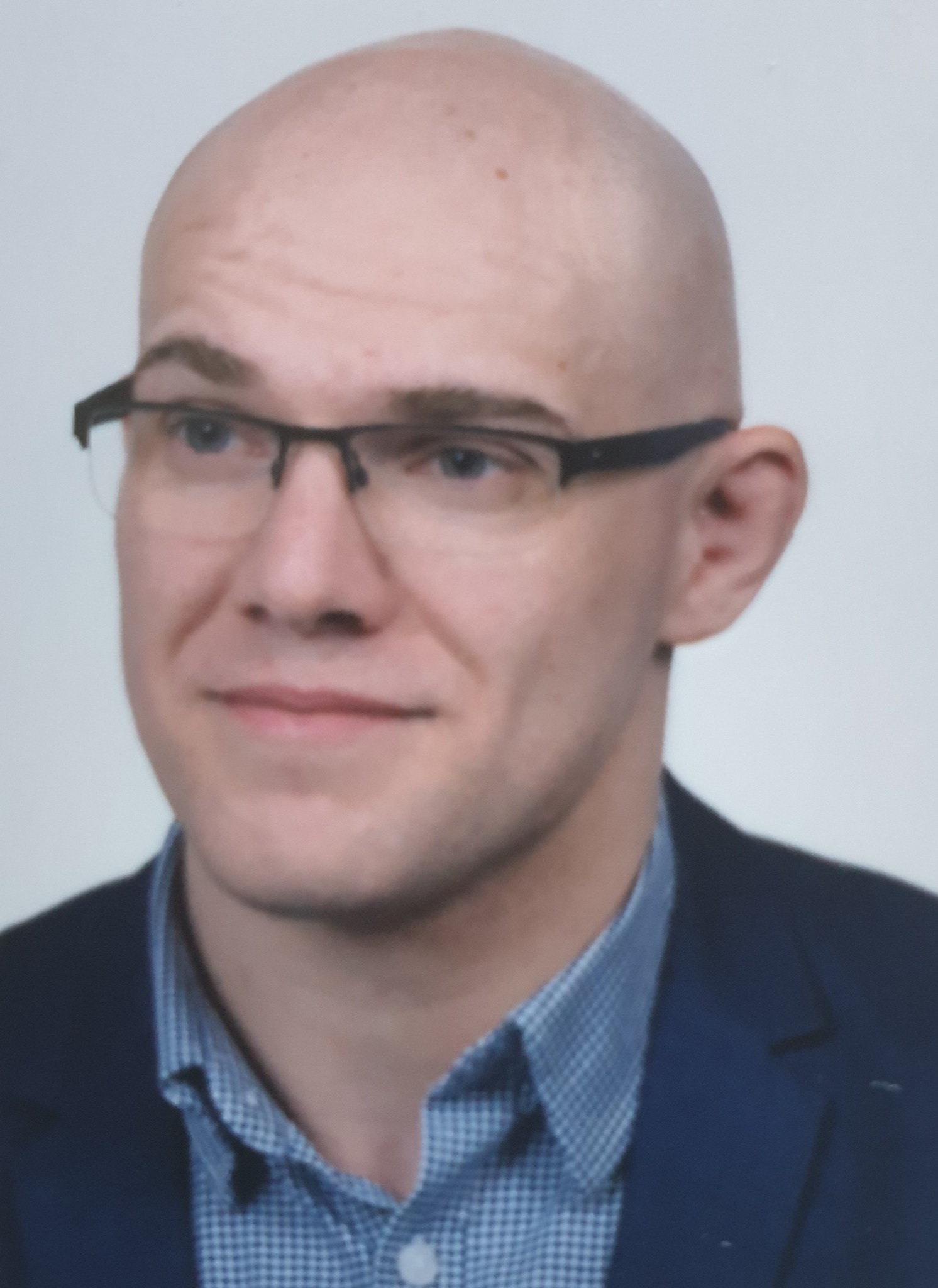 Portret łysiejącego mężczyzny w okularach i niebieskiej marynarce na jasnym tle.