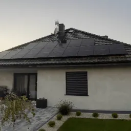 Czarny dach z panelami słonecznymi na jasnym domu jednorodzinnym, widok z boku ogrodu z meblami ogrodowymi i kostką brukową.