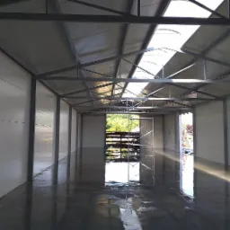 Wnętrze hali przemysłowej w trakcie budowy, widoczne ściany z płyt warstwowych, stalowa konstrukcja dachu z świetlikami, wypoziomowana posadzka przemysłowa oraz rusztowanie w tle.