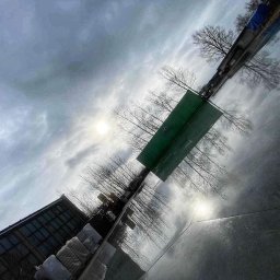 JUR-BUD Jakub Juraszek - Błyszcząca, ciemna posadzka odbija pochmurne niebo, drzewa i fragment budynku, tworząc abstrakcyjne wrażenie głębi.