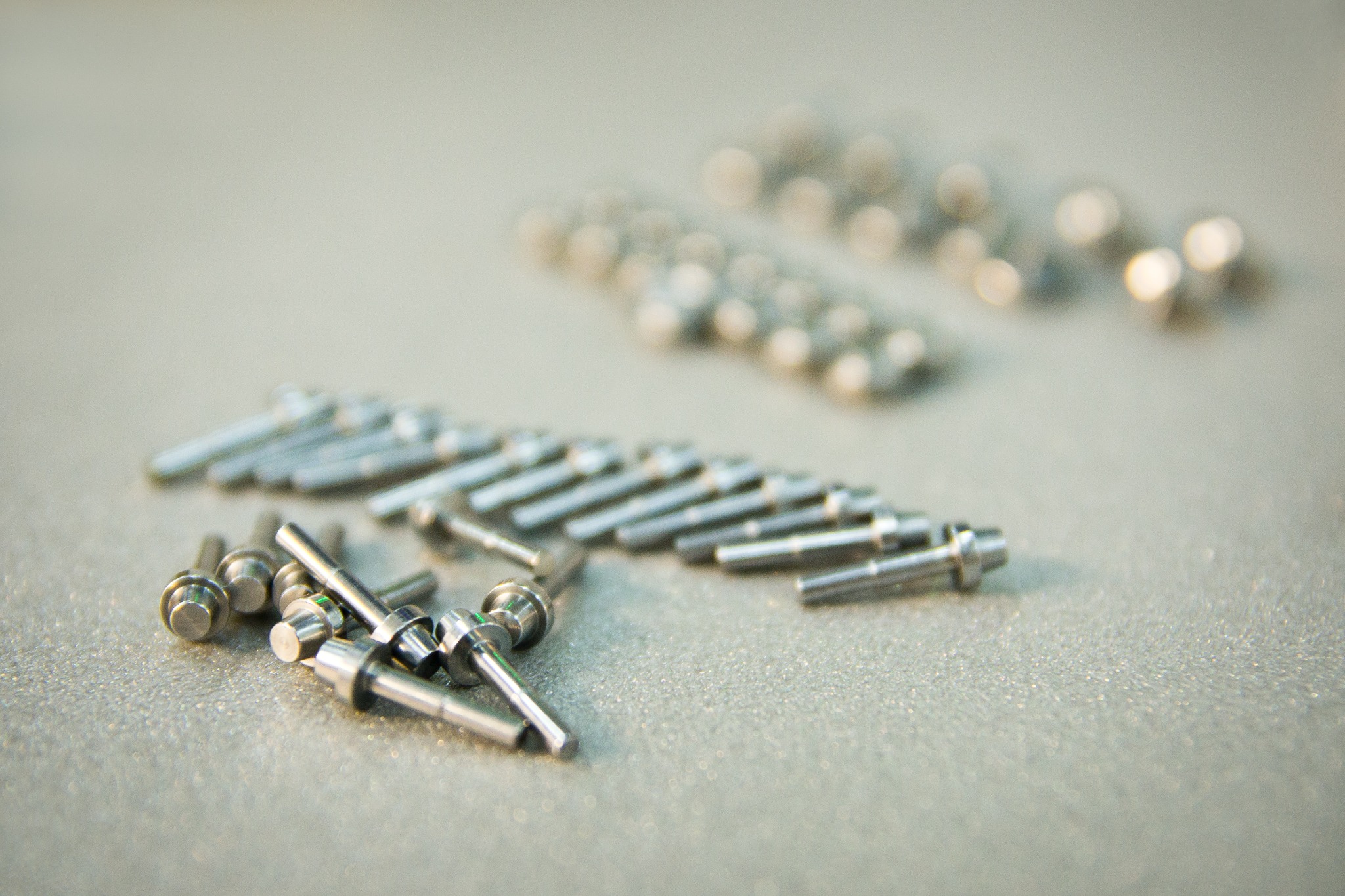Precyzyjnie obrobione, metalowe elementy z widocznymi śladami obróbki, ułożone w rzędach na matowej powierzchni.