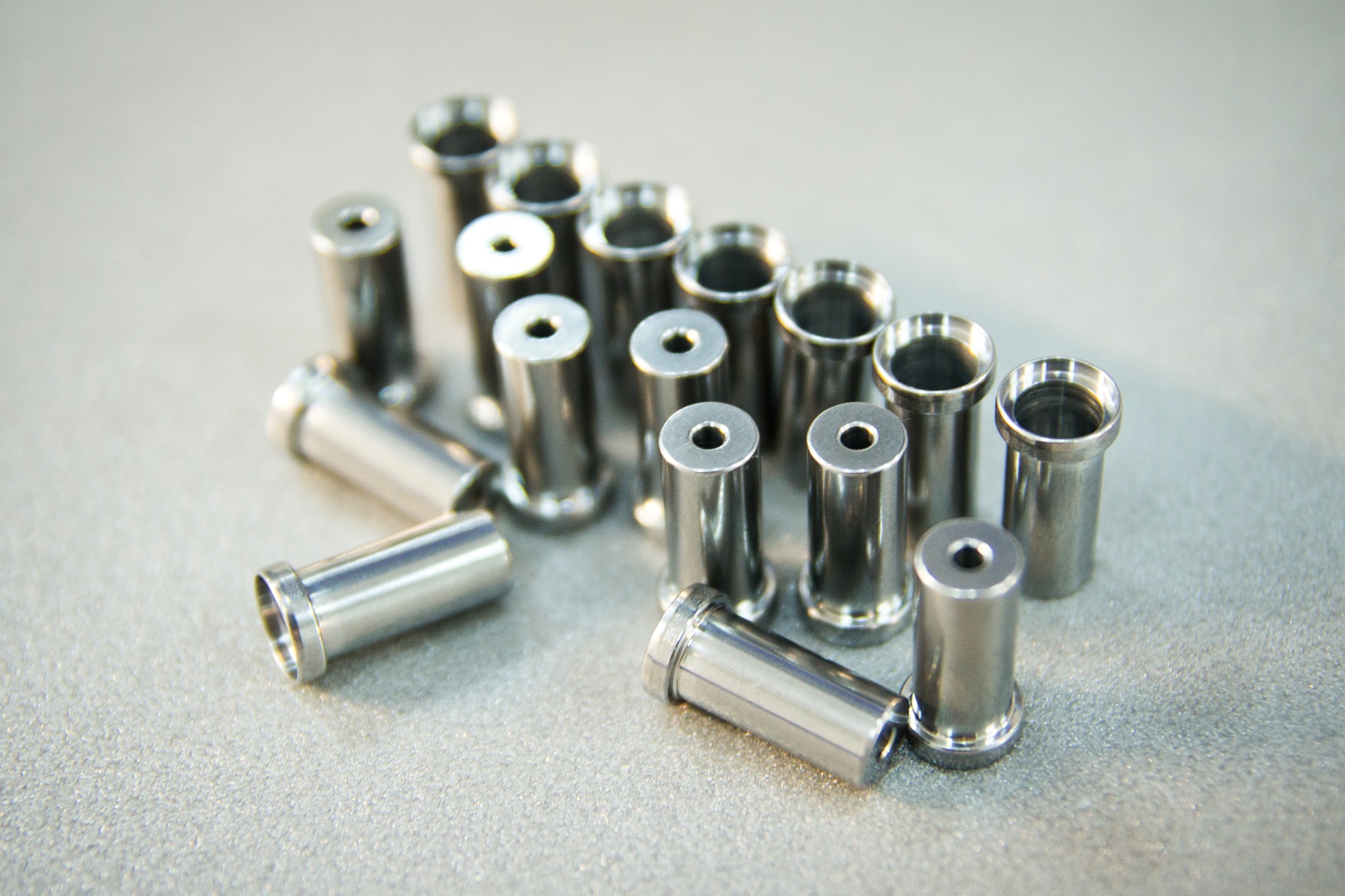 Precyzyjnie wykonane, metalowe tuleje z otworem, ułożone w rzędach na błyszczącej powierzchni, widoczne ślady obróbki CNC.