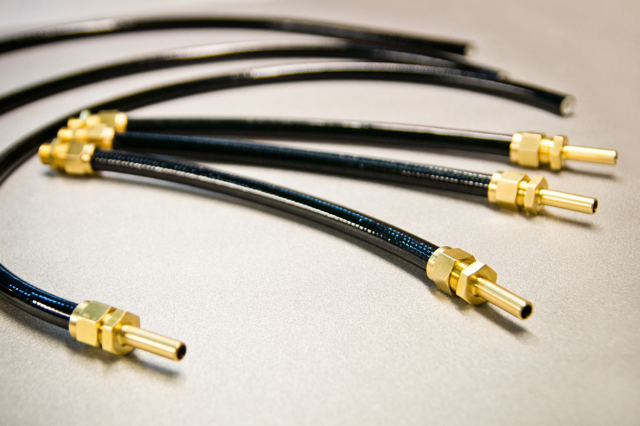 Giętkie, czarne przewody hydrauliczne z mosiężnymi końcówkami na metalowej powierzchni, ułożone równolegle w lekkim łuku.