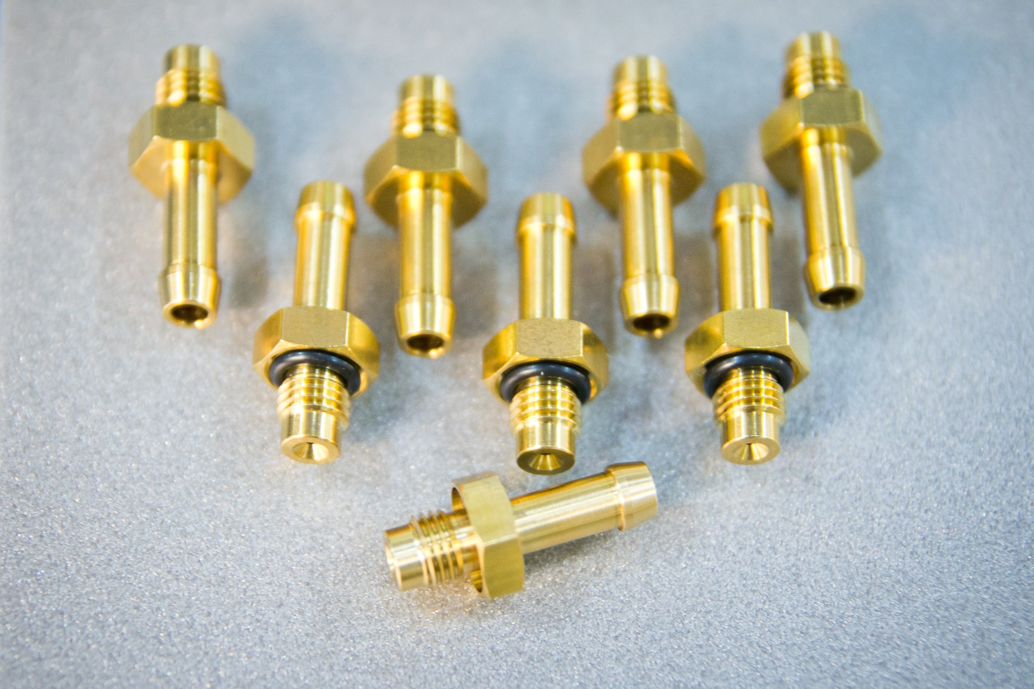 Precyzyjnie wykonane, złote, mosiężne złączki hydrauliczne z gwintami i uszczelkami, ułożone na szarym, teksturowanym tle, prezentujące wysoką jakość obróbki.