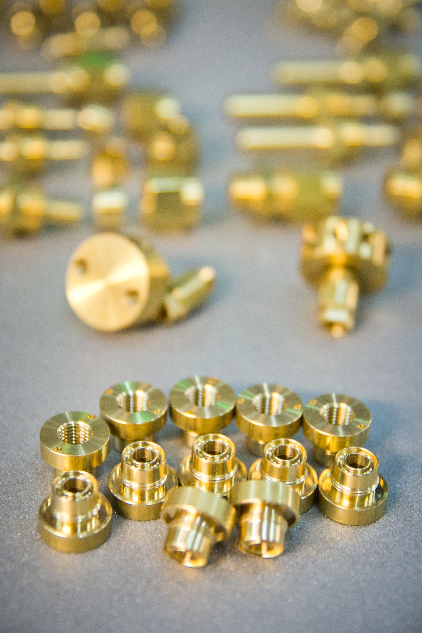 Partie precyzyjnie wykonanych, złotych, metalowych elementów z gwintami i otworami, ułożonych na szarym tle, z rozmytymi detalami w tle.