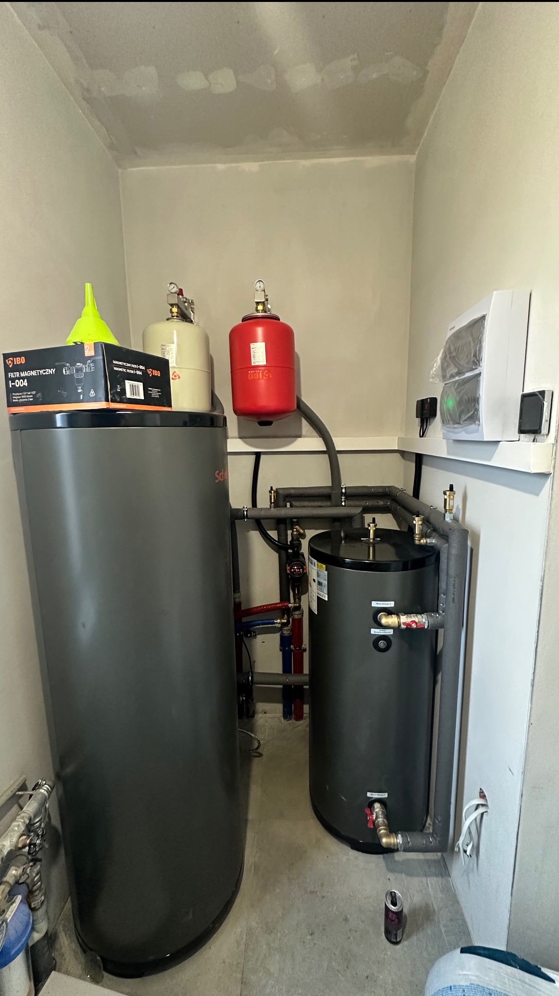 Zestaw dwóch szarych zbiorników z czerwoną i beżową membraną, połączonych rurami. Na większym zbiorniku pudełko filtra magnetycznego IBO i zielony lejek. Widoczne rury i instalacja.