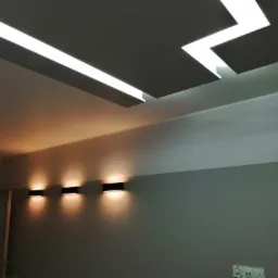 Nowoczesne oświetlenie sufitowe z geometrycznym wzorem i podłużnymi lampami LED, uzupełnione przez trzy czarne kinkiety ścienne emitujące ciepłe światło na szarej ścianie w minimalistycznym wnętrzu.