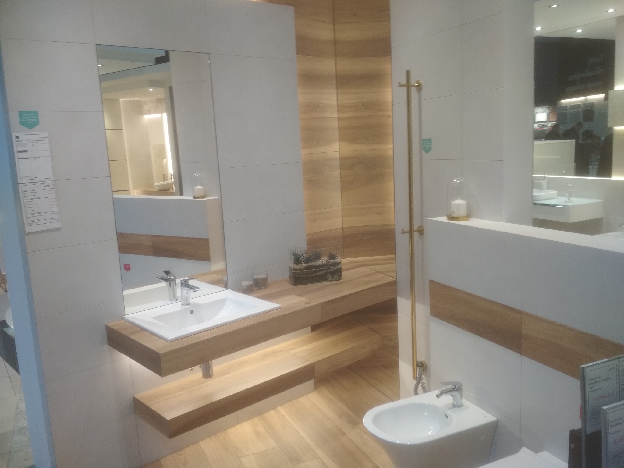 Nowoczesna łazienka z biało-drewnianymi płytkami, wiszącą umywalką na drewnianym blacie z podświetleniem LED, bidetem i dużym lustrem.