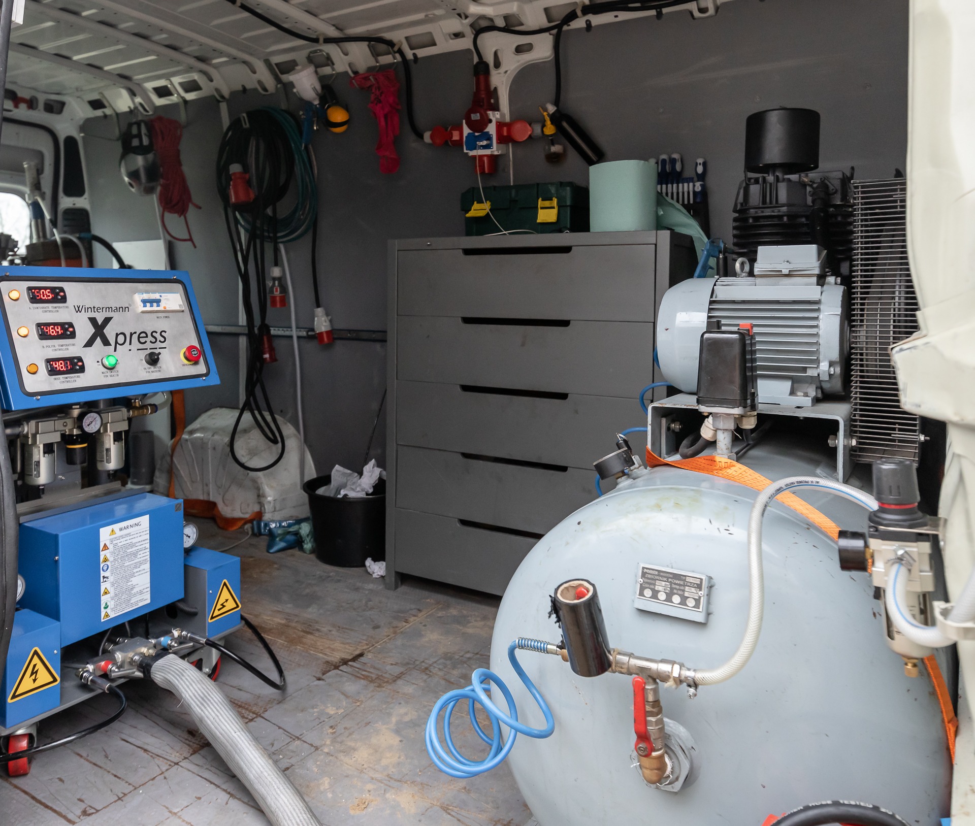 Wnętrze furgonetki z profesjonalnym sprzętem do natrysku, w tym agregat natryskowy Wintermann Xpress, kompresor i szafka z szufladami.