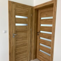 FHU PROFIL DOM Jan Konior - Dwa drewniane skrzydła drzwiowe z poziomymi, matowymi przeszkleniami, zamontowane w białym wnętrzu. Widoczny fragment podłogi z marmurowym wzorem.