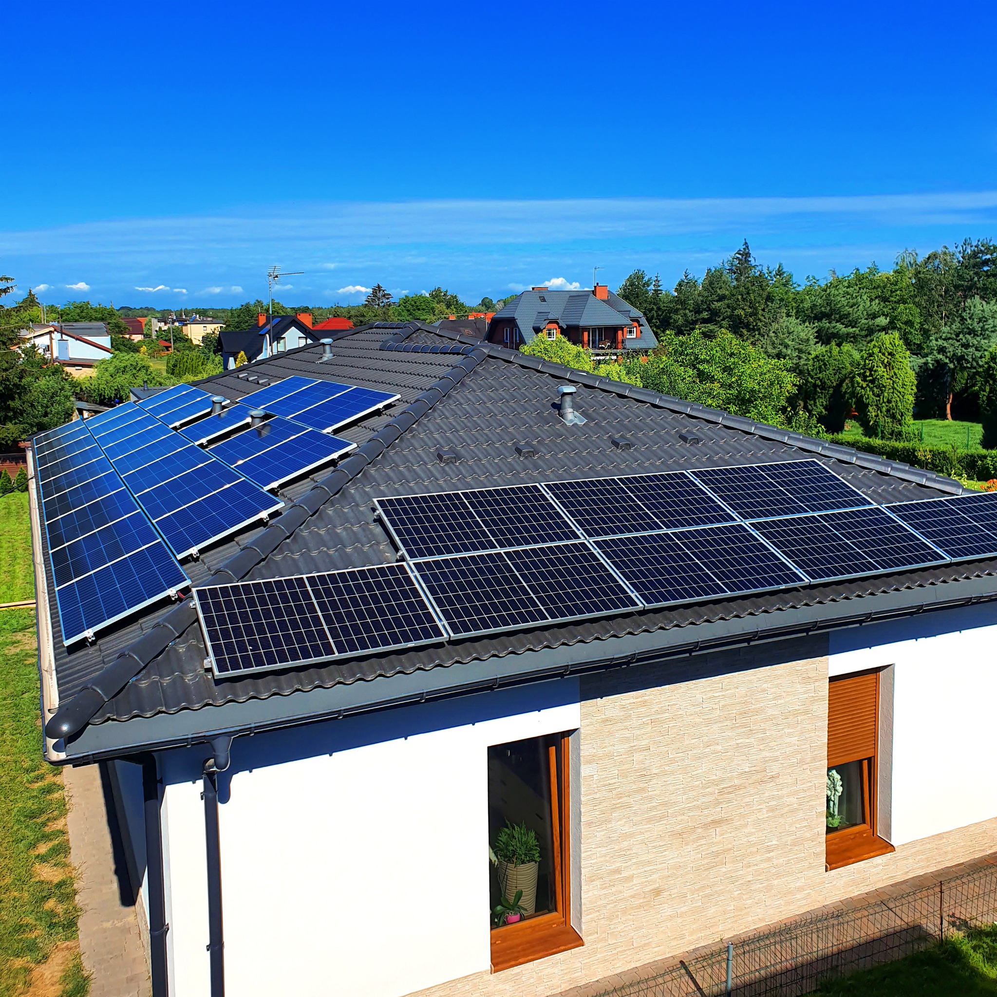 Panele fotowoltaiczne na dachu domu jednorodzinnego z grafitową dachówką, widok z góry w słoneczny dzień.
