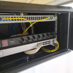 Szafa rack z zamontowanym panelem krosowniczym światłowodowym, listwą zasilającą Lanberg SPD, switchem sieciowym oraz UPS. Żółte kable światłowodowe prowadzą do panela krosowniczego.