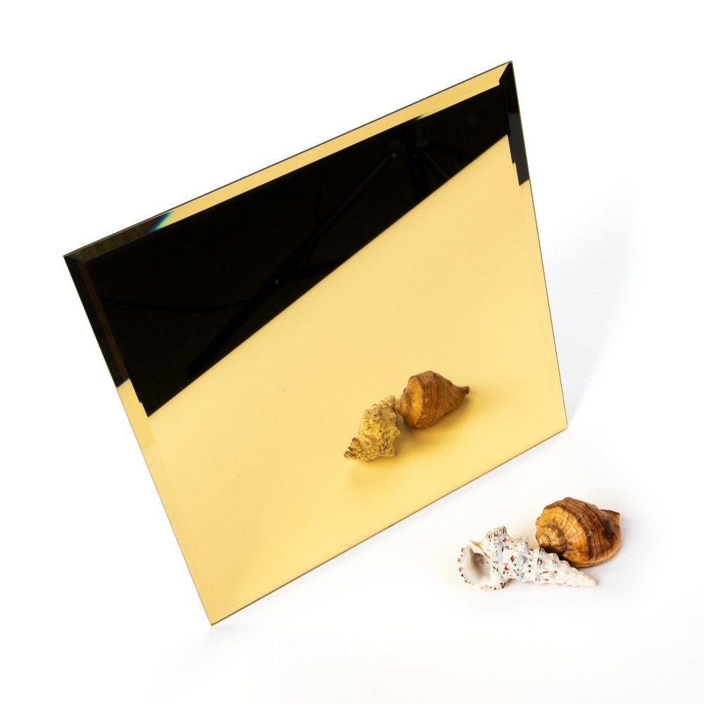 Złota tafla lustra w kształcie trapezu, z trzema muszlami morskimi ułożonymi na białym tle, z widocznym odbiciem statywu w górnej części.