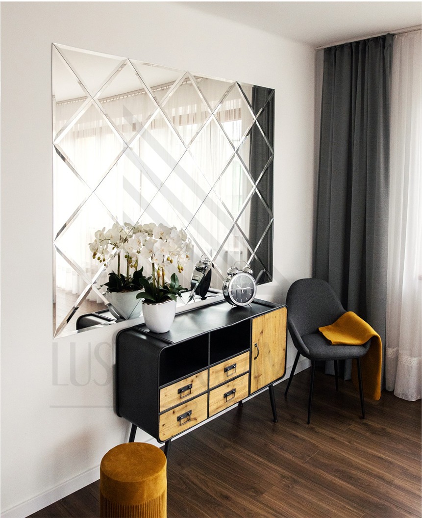 Dekoracyjne lustro ścienne z fazowanych rombów, zamontowane nad komodą w nowoczesnym wnętrzu z szarą zasłoną.