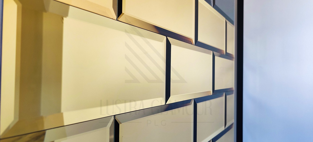 Fragment ściany wyłożonej lustrzanymi płytkami w kształcie cegiełek, z fazowanymi krawędziami, ułożonych w regularny wzór, z widocznym logo firmy w tle.