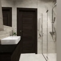 Nowoczesna łazienka z ciemnymi drewnianymi akcentami: szafka pod umywalką z czarnym blatem, biała umywalka nablatowa, lustro, ciemne drzwi, kabina prysznicowa z deszczownicą i biały ręcznik.