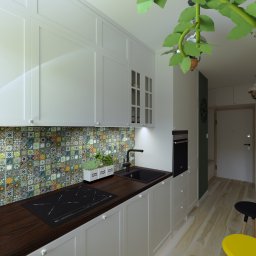 EF-KA Studio Design EWA WESOŁEK-PRZYCHODZKA - Wizualizacja kuchni z białymi szafkami, drewnianym blatem, kolorową mozaiką na ścianie, czarnym zlewem i płytą indukcyjną. Na blacie doniczka z ziołami. Widoczny fragment salonu z zieloną ścianą...