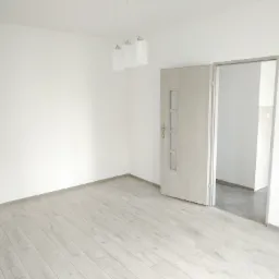 Jasne panele podłogowe imitujące drewno w pustym, nowym pokoju z otwartymi, wewnętrznymi drzwiami i wiszącą lampą z trzema kloszami.