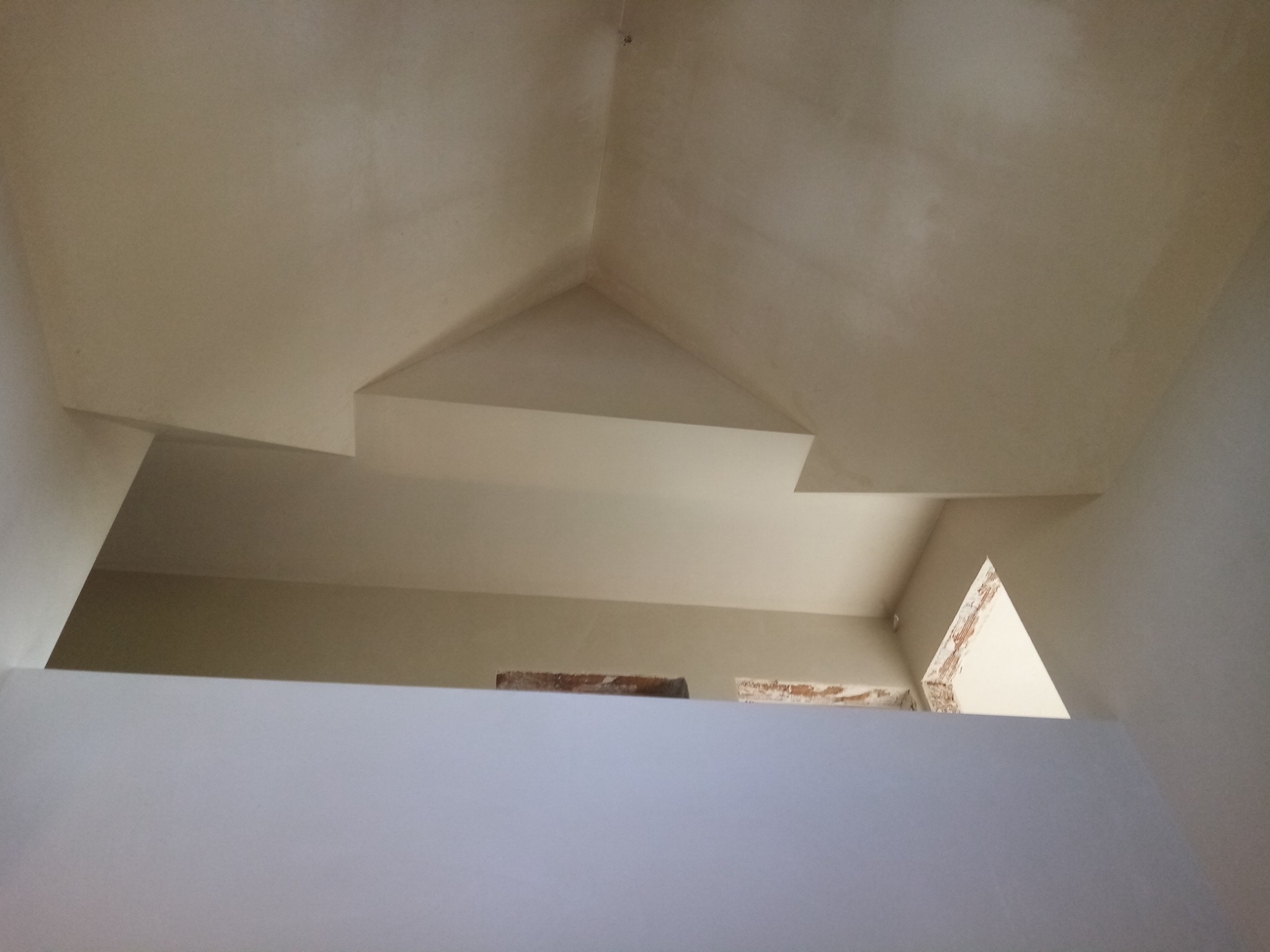 Wnętrze wiatrołapu po nałożeniu gładzi gipsowej, widok z dołu na skos sufitu i fragment ściany z widocznymi fragmentami cegieł.