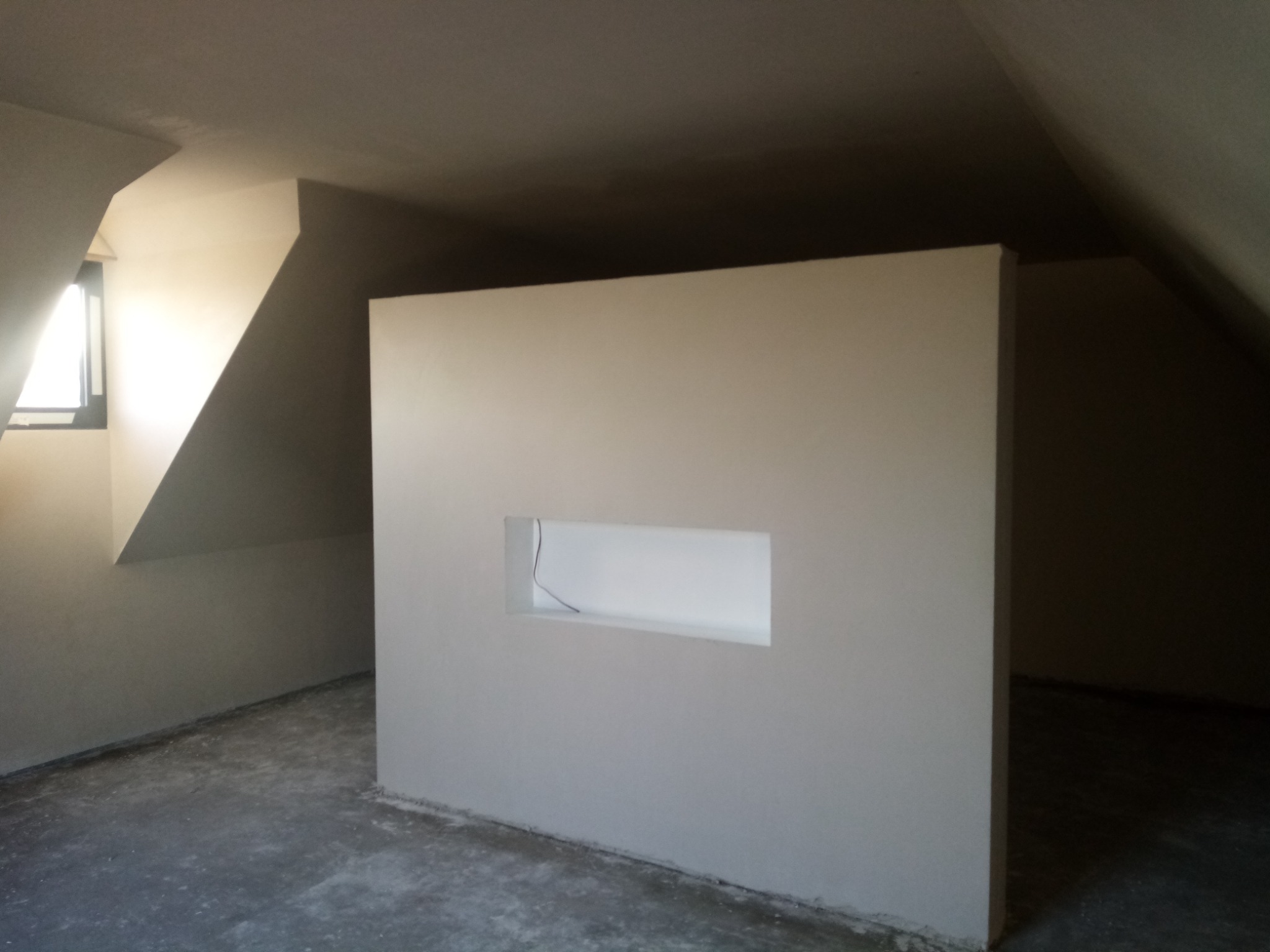 Poddasze po nałożeniu gładzi, widoczna ściana działowa z wnęką na instalację elektryczną, szare podłoże w trakcie prac wykończeniowych.
