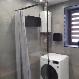 Szara łazienka z kabiną prysznicową z zasłoną, piecykiem gazowym, półkami i pralką LG.