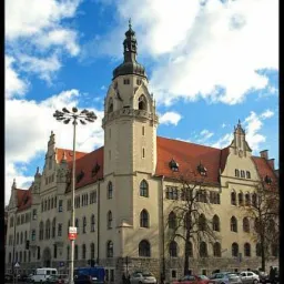 Budynek sądu z wieżą na tle błękitnego nieba z chmurami, z zaparkowanymi samochodami i ulicą na pierwszym planie.