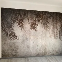 Ściana z fototapetą przedstawiającą motyw palm, widoczny fragment drabiny malarskiej, szare panele podłogowe.